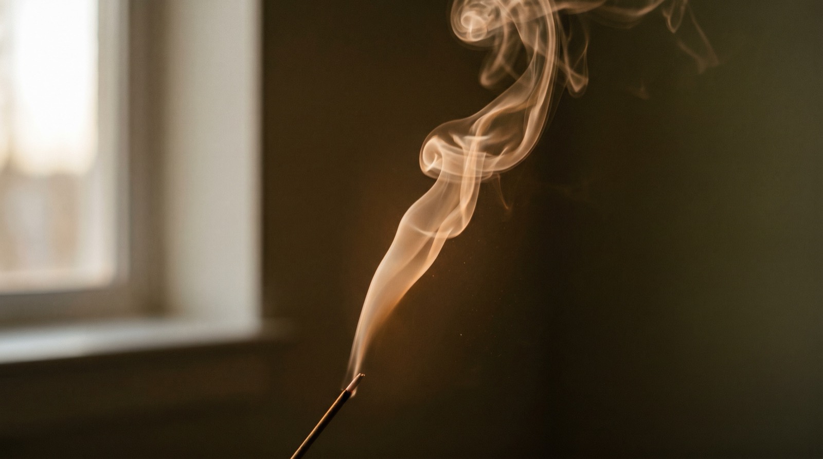 A single thread of incense smoke rising in soft warm light